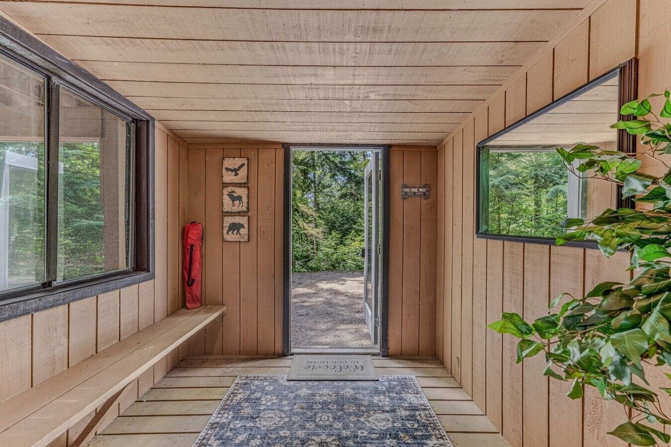 A wooden interior with a bench, a red bag, and a door leading outside.