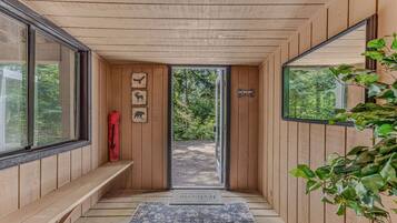 A wooden interior with a bench, a red bag, and a door leading outside.