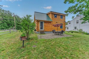 A log cabin with a patio, a small table with chairs, and a covered umbrella. - Private Riverfront Access in the heart of Lincoln (Lincoln)
