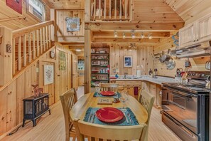 A wooden interior with a dining table set for four, a kitchen with modern appliances, and a staircase leading to an upper level. - Private Riverfront Access in the heart of Lincoln (Lincoln)