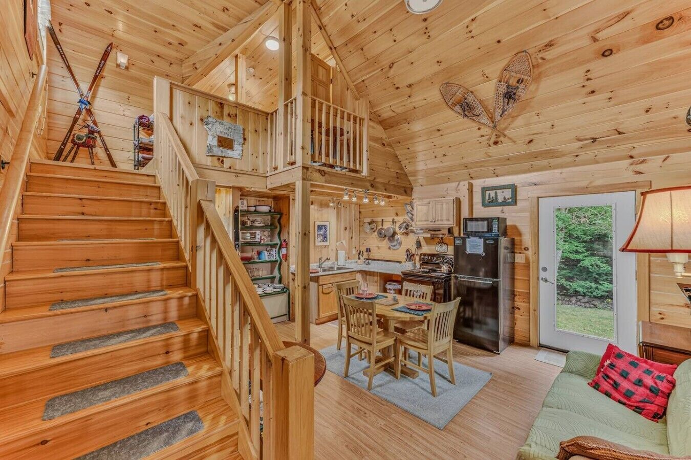 A wooden cabin interior with a staircase, kitchen, dining area, and a cozy living space.