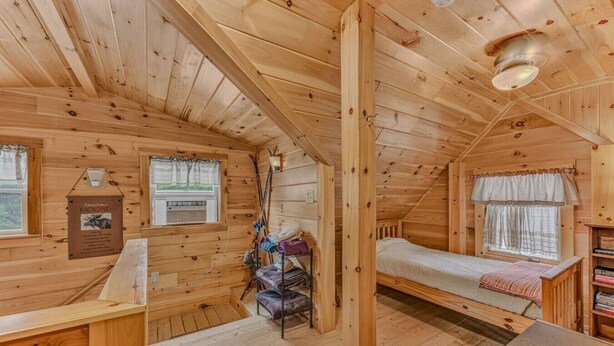 Een houten hutje met een bedstee, een klein bureau en een raam met gordijnen.