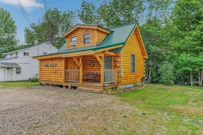 A log cabin with a porch, a covered outdoor seating area, and a visible name plaque.