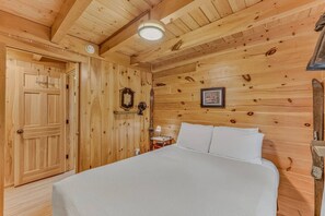 A wooden room with a bed, a door, and a wall-mounted light fixture.