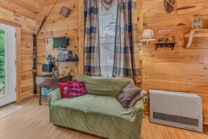 A cozy cabin interior with a green sofa, a television, and a window with curtains. - Private Riverfront Access in the heart of Lincoln (Lincoln)