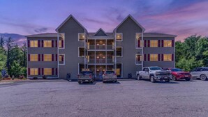 A multi-story hotel with a symmetrical facade, a central entrance, and a parking lot with several vehicles. - Luxe Condo at Forest Ridge- Amenities & Central AC (Lincoln)