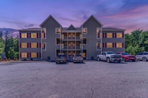 Ein mehrstöckiges Hotel mit symmetrischer Fassade, einem zentralen Eingang und einem Parkplatz mit mehreren Fahrzeugen.