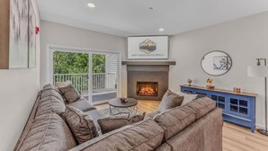 A modern living room with a fireplace, a sofa set, a dining table, and a blue cabinet. - Luxe Condo at Forest Ridge- Amenities & Central AC (Lincoln)