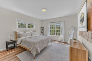 Ein Schlafzimmer mit einem Bett, Nachttischen, einem Fenster mit Vorhängen, einem gerahmten Bild an der Wand und einem Holzboden.