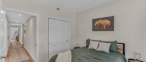 A bedroom with a bed, a door, a hallway, and a wall-mounted picture.