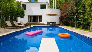 Ein Swimmingpool mit Liegestühlen und einem Tisch, umgeben von Bäumen und einem Gebäude.