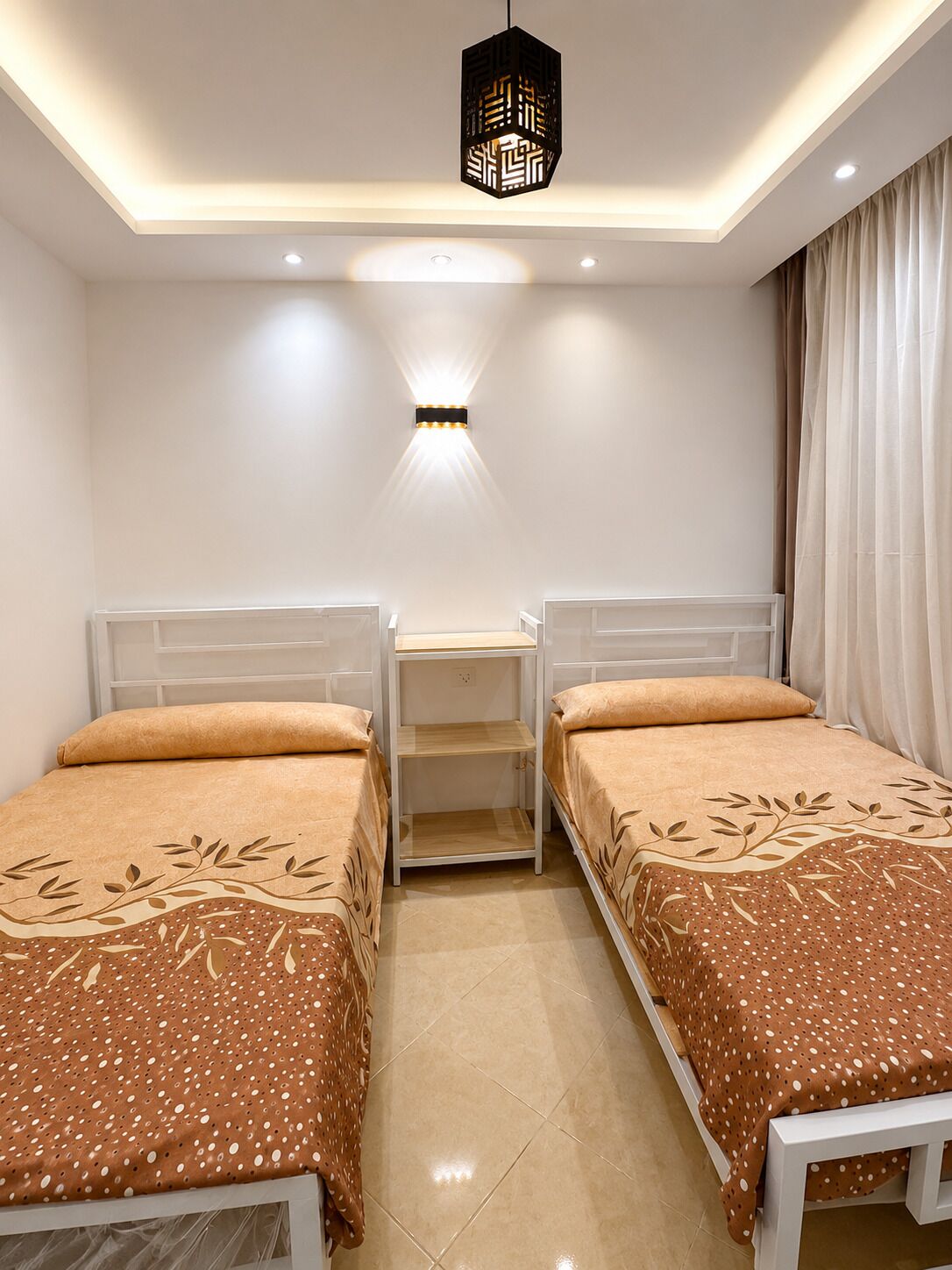 Une chambre avec deux lits simples, une table de chevet, une lampe fixée au mur et un luminaire au plafond.