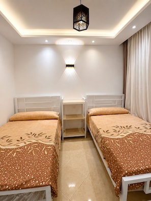 Une chambre avec deux lits simples, une table de chevet, une lampe fixée au mur et un luminaire au plafond.