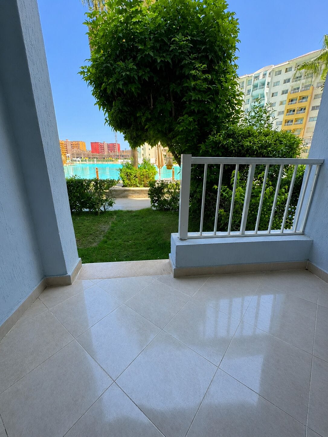 Un balcon donnant sur une piscine, une pelouse et un arbre.