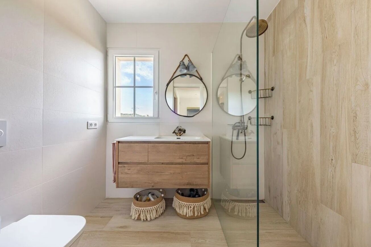 A modern bathroom with a wooden vanity, a glass shower enclosure, and a large mirror.