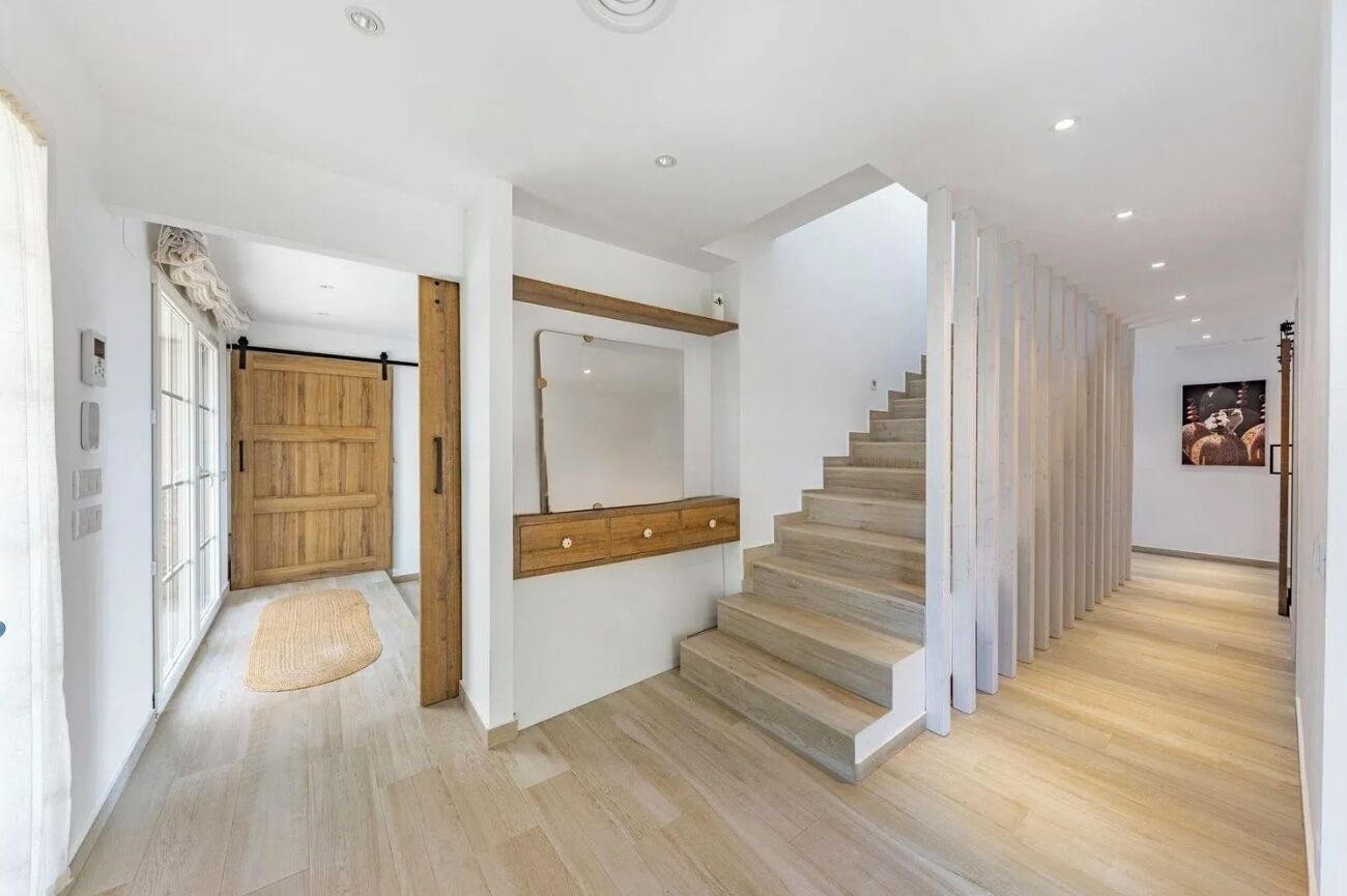 Un interior moderno con una escalera, una puerta de madera y un espejo.