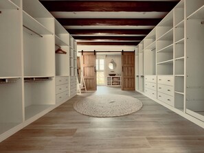 Un vestidor amplio con vigas de madera, estanterías abiertas y una alfombra central.