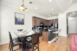 A modern kitchen with dark wood cabinets, a central island, and a dining area with a table and chairs. - Afrotique HOU Getaway Pool!Galleria!Uptown (Houston)