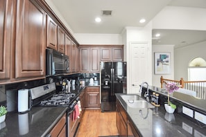 A modern kitchen with dark wood cabinets, stainless steel appliances, and a central island with a sink. - Afrotique HOU Getaway Pool!Galleria!Uptown (Houston)