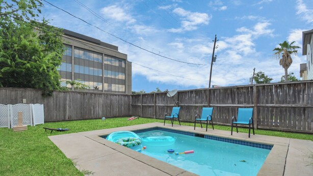 A backyard with a swimming pool, a wooden fence, and a building in the background. - Afrotique HOU Getaway Pool!Galleria!Uptown (Houston)