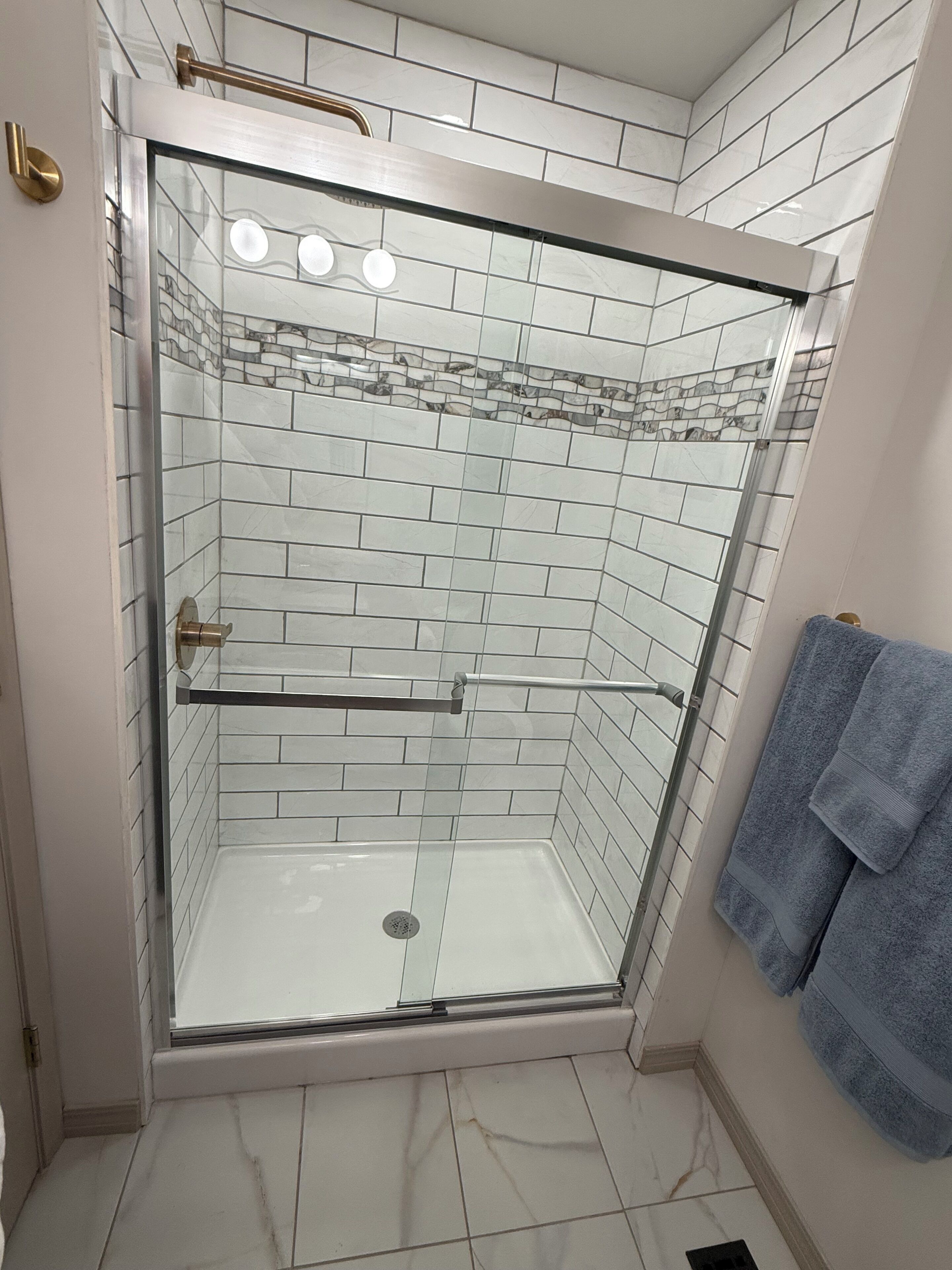 A glass-enclosed shower with white tiles and a marble floor.