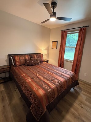 A bedroom with a bed, a ceiling fan, a window with curtains, and a bedside lamp.