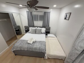 Ein Schlafzimmer mit Bett, Nachttischen, Deckenventilator, Kleiderschrank und einem Fenster mit Vorhängen.
