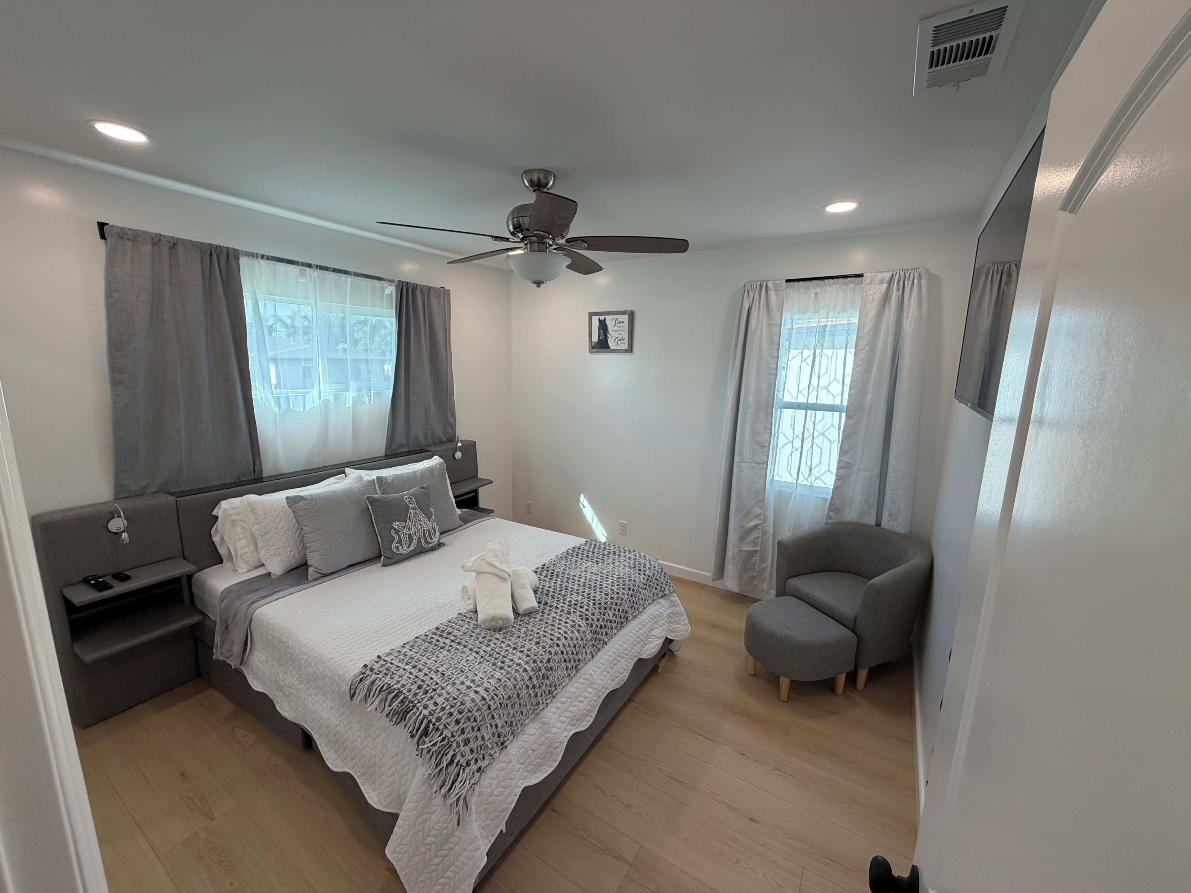 Une chambre moderne avec un lit, des tables de chevet, une chaise et un ventilateur de plafond.