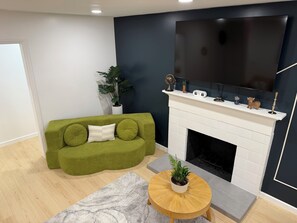 Ein modernes Wohnzimmer mit einem grünen Sofa, einem weißen Kamin und einem an der Wand befestigten Flachbildfernseher.