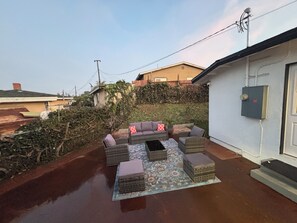 Eine Terrasse mit Gartenmöbeln, einem gemusterten Teppich und einem Haus im Hintergrund.