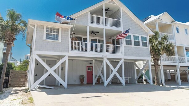 Ein zweistöckiges Strandhaus mit Balkon, einer roten Tür und einer Flagge.