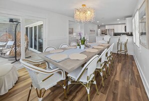 A dining area with a long table, white wicker chairs, and a chandelier. - 6BR, POOL, 2 min walk to beach, Oceanview, Game Rm (Carolina Beach)