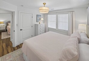 A bedroom with a large bed, a dresser, a nightstand, and a window with blinds. - 6BR, POOL, 2 min walk to beach, Oceanview, Game Rm (Carolina Beach)