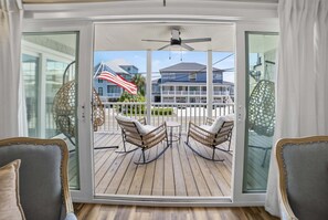A room with a sliding glass door leading to an outdoor deck with wicker furniture and a view of a house with an American flag. - 6BR, POOL, 2 min walk to beach, Oceanview, Game Rm (Carolina Beach)