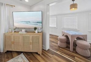 A room with a wooden cabinet, a television, a table with chairs, and a hanging light fixture. - 6BR, POOL, 2 min walk to beach, Oceanview, Game Rm (Carolina Beach)