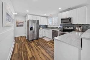 A modern kitchen with white cabinets, stainless steel appliances, and a wooden floor. - 6BR, POOL, 2 min walk to beach, Oceanview, Game Rm (Carolina Beach)