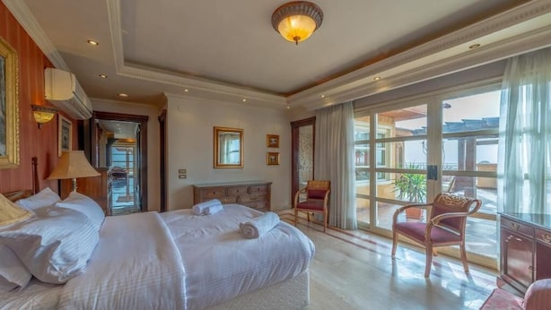A hotel room with two beds, a sitting area with a chair, and a large window offering a view.