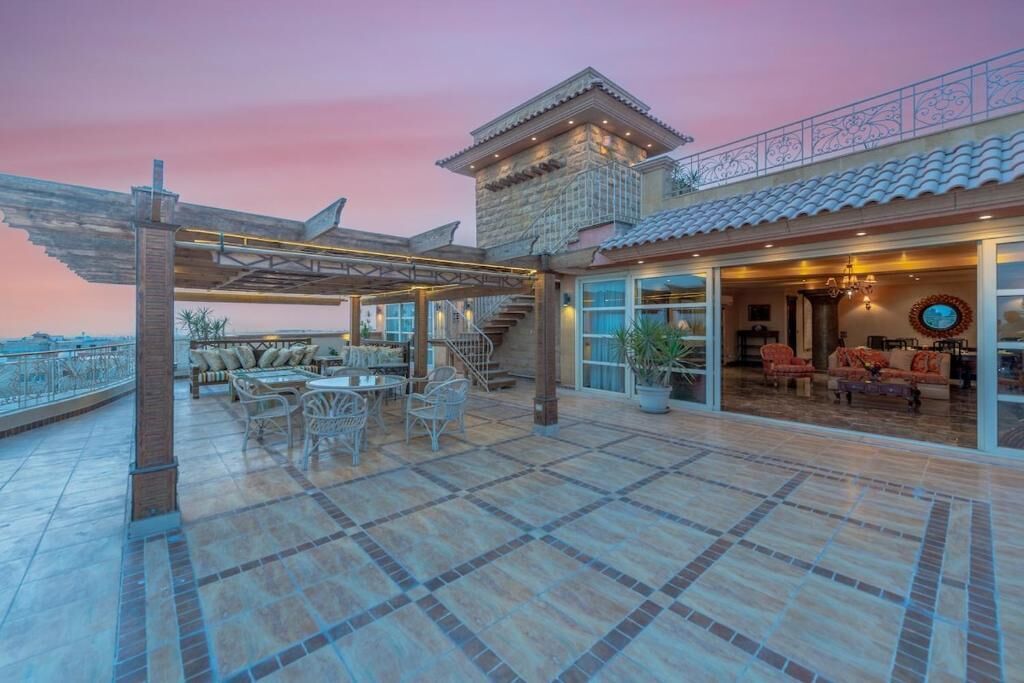 A spacious outdoor patio with a covered seating area, a stone building with a tiled roof, and a view of the surrounding landscape.