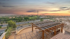 A rooftop terrace with a view of a cityscape at sunset.