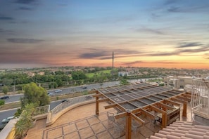A rooftop terrace with a view of a cityscape at sunset.