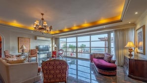 A spacious living room with a large window, a chandelier, and a variety of seating options.