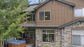 A two-story house with a stone facade, large windows, and a hot tub in the backyard.