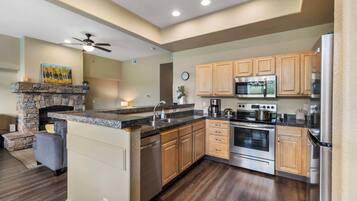 A modern kitchen with a stone fireplace, wooden cabinets, stainless steel appliances, and a large island.