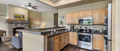 A modern kitchen with a stone fireplace, wooden cabinets, stainless steel appliances, and a large island.