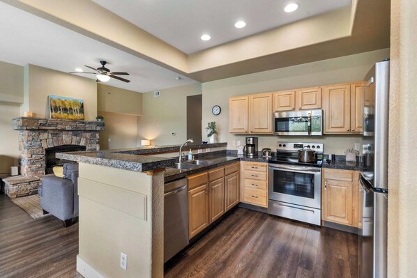A modern kitchen with a stone fireplace, wooden cabinets, stainless steel appliances, and a large island.