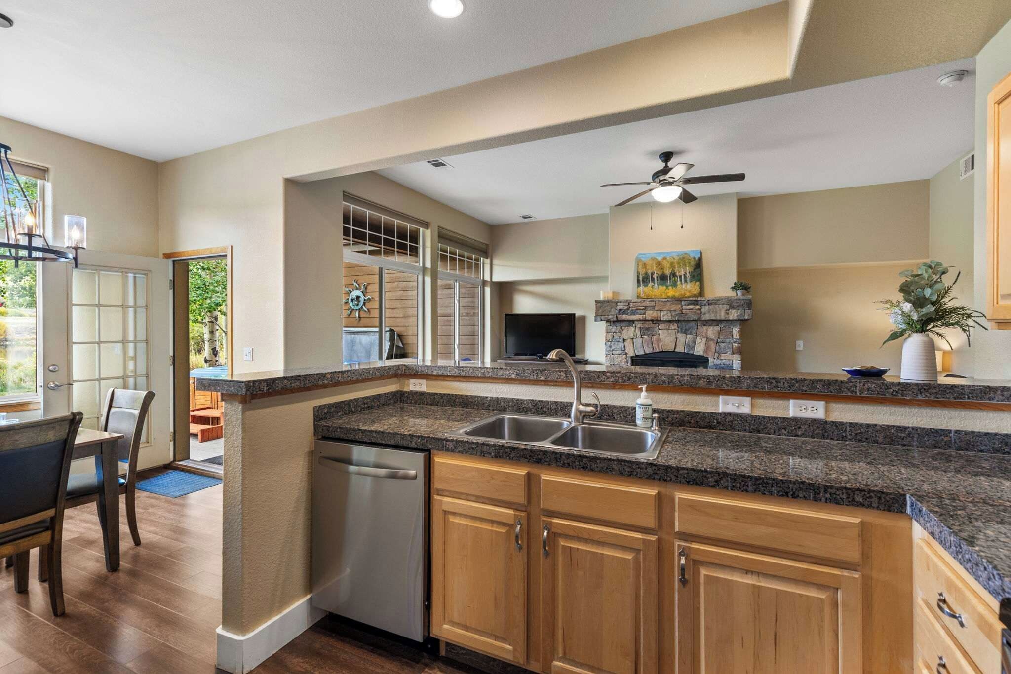 A kitchen with granite countertops, wooden cabinets, a dishwasher, and a stone fireplace.