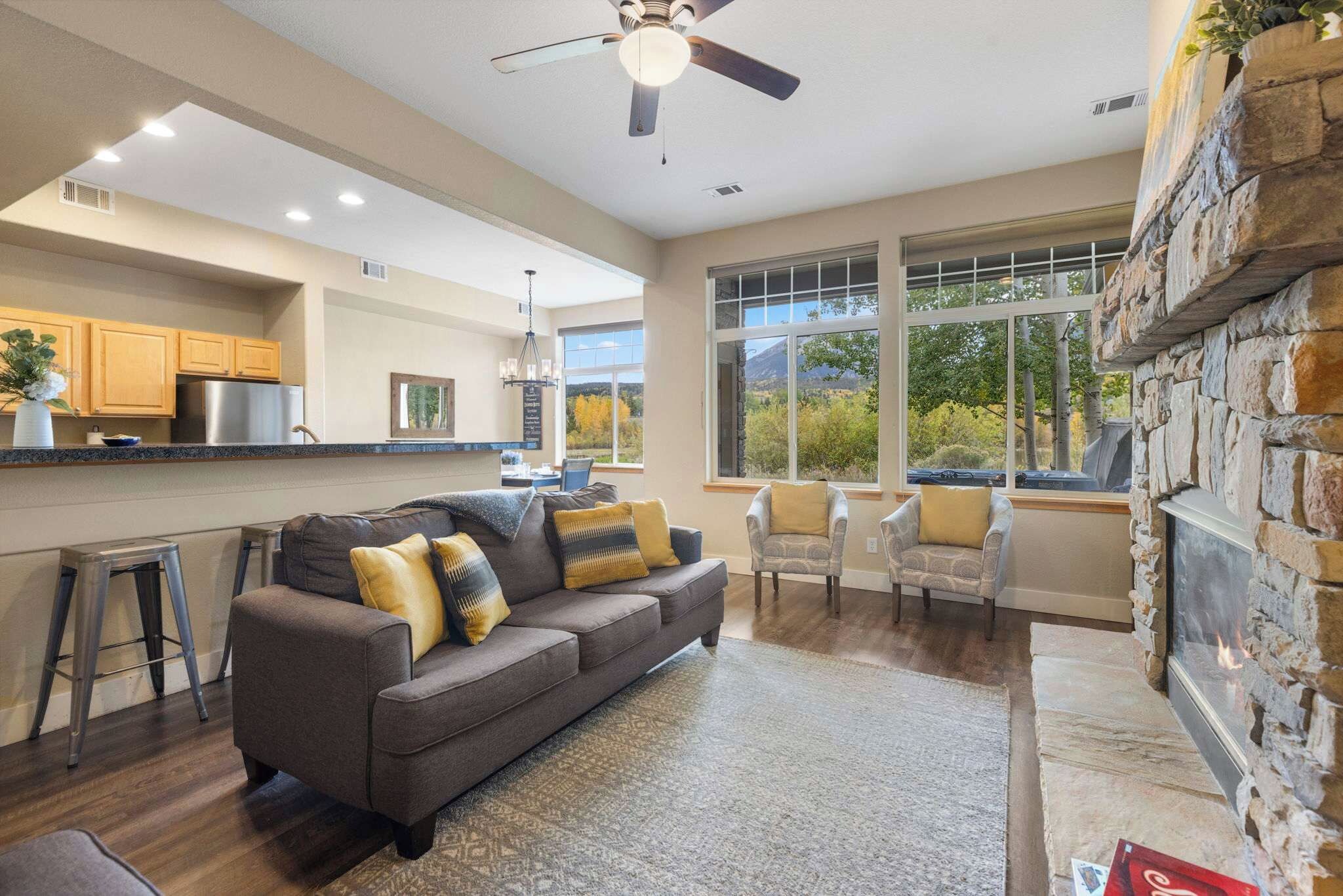 A modern living room with a gray sofa, two armchairs, and a stone fireplace.