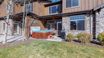 A two-story house with a stone exterior, a wooden deck, and a hot tub in the backyard.