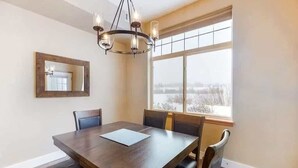 Ein Esszimmer mit großem Tisch, Stühlen, einer Chandelieber, einem Fenster mit Aussicht und einem Spiegel an der Wand.