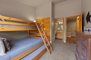 A bunk bed with a wooden ladder, a dresser, and a bathroom visible through an open door.